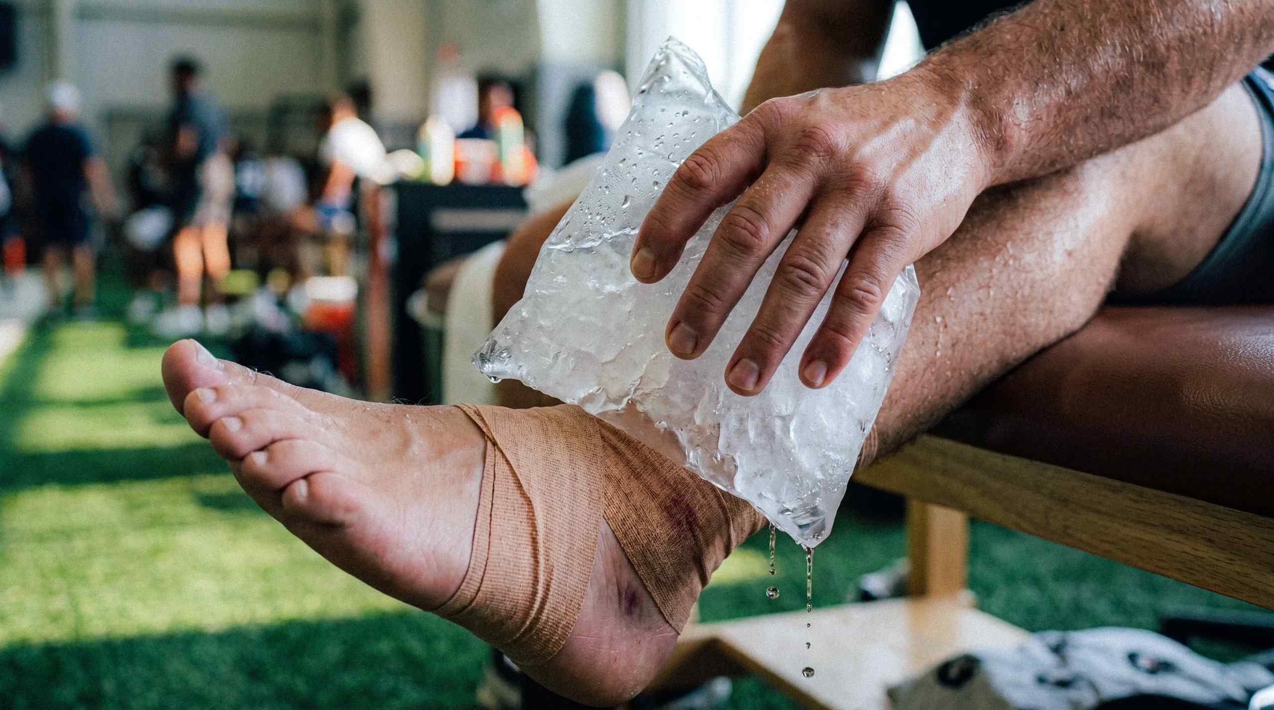 An athlete icing down his ankle, which is wrapped in tape.